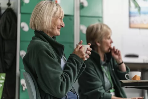 A smiling food bank volunteer holding a cup of tea.